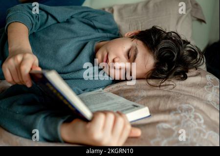 Ein Junge, der zu Hause auf dem Bett liegt und einen Roman liest Stockfoto