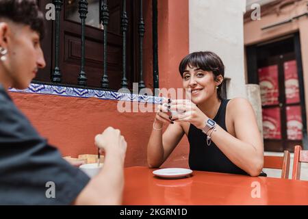 Lächelnde Frau mit Kaffeetasse, die mit ihrem Freund im Straßencafé sitzt Stockfoto