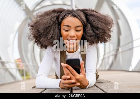Lächelnde Frau, die auf der Fußgängerbrücke auf ein Smartphone schaut Stockfoto