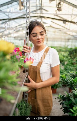 Gärtner mit geschlossenen Augen, der sich im Gewächshaus auf ein Regal lehnt Stockfoto