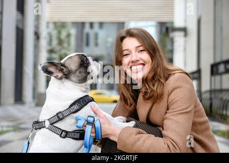 Glückliche Frau, die französische Bulldogge auf dem Fußweg streichelt Stockfoto