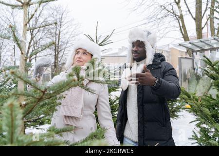 Junger Mann mit Frau, die Weihnachtsbaum im Schnee kauft Stockfoto