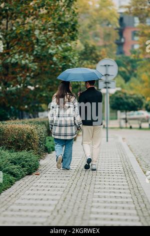 Ein junges Paar, das unter dem Schirm auf dem Fußweg spaziert Stockfoto