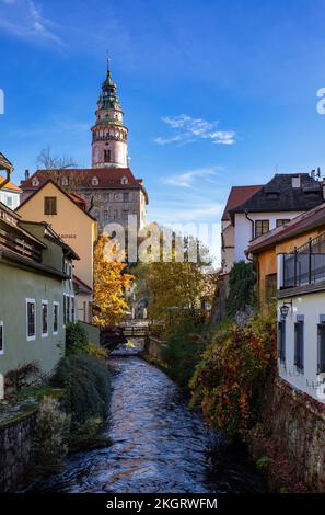 Tschechische Republik, Südböhmische Region, Cesky Krumlov, Fluss fließt zwischen alten Stadthäusern mit dem Turm der Burg Cesky Krumlov im Hintergrund Stockfoto