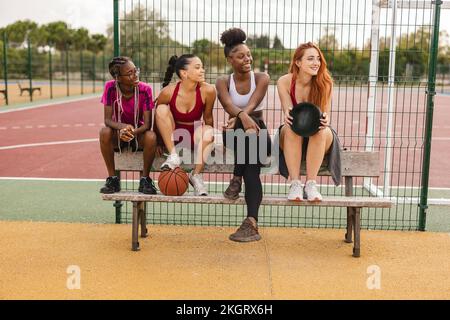 Glückliche Freunde sitzen auf der Bank am Sportplatz Stockfoto