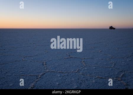 Geländewagen und Personen, die in der Nähe auf der Salar de Uyuni (Uyuni Salzplatte) bei Sonnenaufgang, Potosi Department, Bolivien Stockfoto