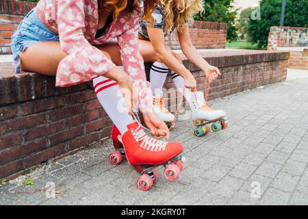 Frauen, die an der Wand sitzen und Rollschuhspitzen binden Stockfoto