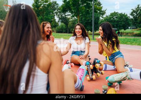 Fröhliche Freunde, die Rollschuhe tragen und sich auf dem Sportplatz unterhalten Stockfoto