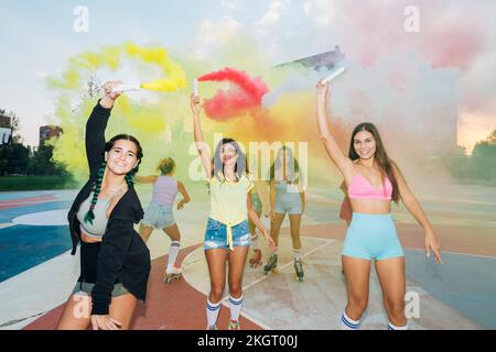 Fröhliche Freunde spielen mit Rauchfarben und Rollschuhlaufen auf dem Sportplatz Stockfoto