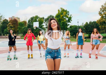 Glückliche junge Frau vor Freunden, die Rollschuhlaufen auf dem Sportplatz trägt Stockfoto