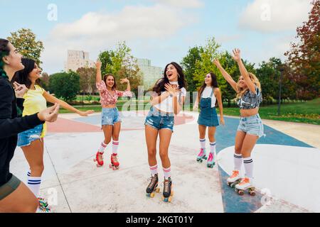 Glückliche junge Frau mit Freunden, die Rollschuhlaufen und auf dem Sportplatz tanzen Stockfoto