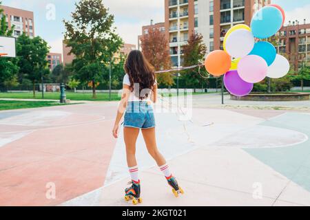 Junge Frau mit bunten Ballons beim Rollschuhlaufen auf dem Sportplatz Stockfoto