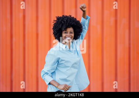 Fröhliche junge Frau, die vor der orangefarbenen Wand tanzt Stockfoto