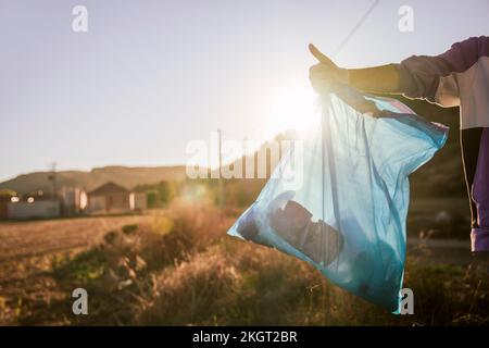 Eine Frau mit Müllsack, die bei Sonnenuntergang die Daumen nach oben zeigt Stockfoto