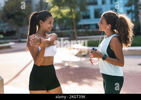 Lächelndes Teenager-Mädchen, das an sonnigen Tagen Sport macht und mit einer Freundin spricht Stockfoto