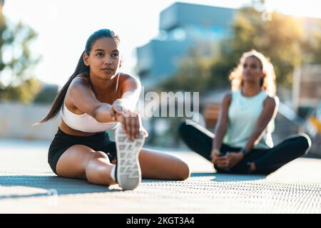 Teenager-Mädchen, die an sonnigen Tagen Stretching-Übungen mit einem Freund im Hintergrund üben Stockfoto