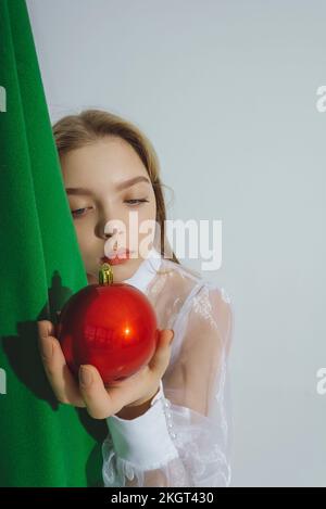 Ein Mädchen sieht sich rote Weihnachtsschmuck vor weißem Hintergrund an Stockfoto