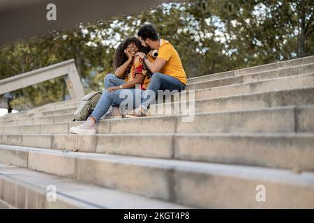 Glückliches junges Paar, das auf den Stufen sitzt und seine Freizeit zusammen verbringt Stockfoto
