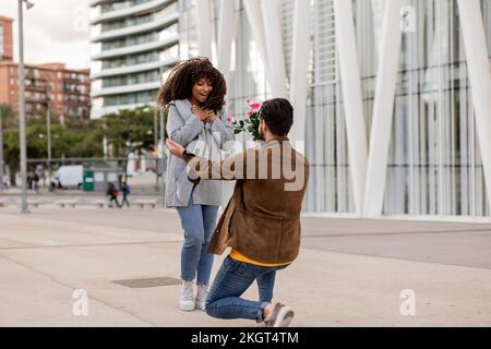 Ein junger Mann, der eine Frau mit Blumenstrauß vorschlägt Stockfoto