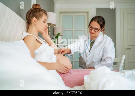 Arzt untersucht schwangere Frau, die zu Hause im Bett sitzt Stockfoto