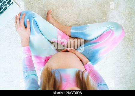 Schwangere Frau, die zu Hause auf dem Teppich sitzt Stockfoto