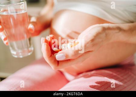 Schwangere Frau hält Pillen und Trinkwasser in der Hand Stockfoto