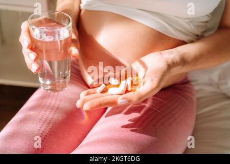 Schwangere Frau hält Pillen und Trinkwasser in der Hand Stockfoto