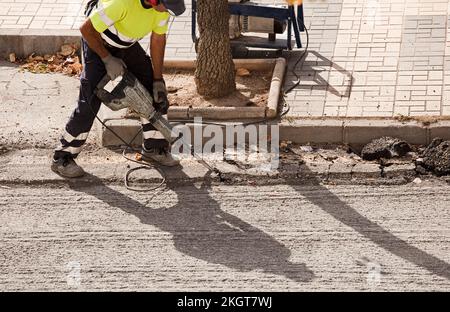 Der Bediener bohrt mit dem Hammer den Untergrund, um den neuen Asphalt zu montieren Stockfoto