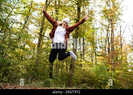 Eine sorgenfreie, reife Frau, die im Wald vor Bäumen hüpft Stockfoto