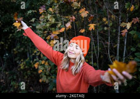 Reife Frau, die Herbstblätter hält, mit geschlossenen Augen im Wald Stockfoto