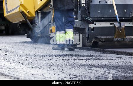 Fahrer und Straßenbaumaschinen, frisch verlegter neuer Asphalt Stockfoto