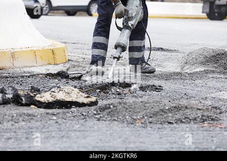 Der Bediener bohrt mit dem Hammer den Untergrund, um den neuen Asphalt zu montieren Stockfoto