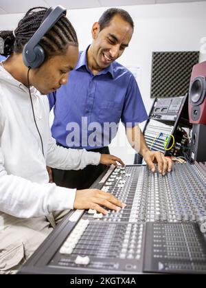 Musikschüler: Audio-Mixer. Ein junger Toningenieur, der mit seinem Lehrer die Verwendung eines Mixpults in einem Musikstudio lernt. Aus einer Reihe von zugehörigen Bildern. Stockfoto