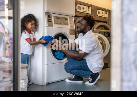 Der Mann und seine Tochter legen Wäsche in die Waschmaschine Stockfoto