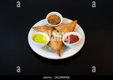 Indische Dishe kulinarisches Still Life. Samoussa mit scharfen Saucen, serviert auf einem Teller Stockfoto