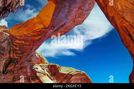 Niedriger Winkel Blick auf roten Sandsteinbrückenbogen vor blauem Himmel, flauschige Sommerwolken - Double Arch, Arches Nationalpark, Utah Stockfoto