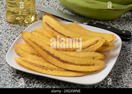 Gericht mit frisch geschnittenen und gebackenen Bananenchips aus nächster Nähe und frischen grünen Mehlbananen im Hintergrund Stockfoto