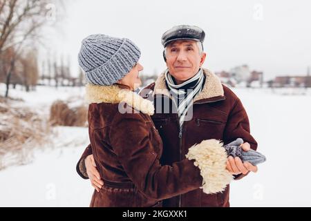 Älteres Familienpaar tanzt im Freien bei schneebem Winterwetter. Ältere Menschen, die ein romantisches Date haben, gehen im Park spazieren. Valentinstag Stockfoto
