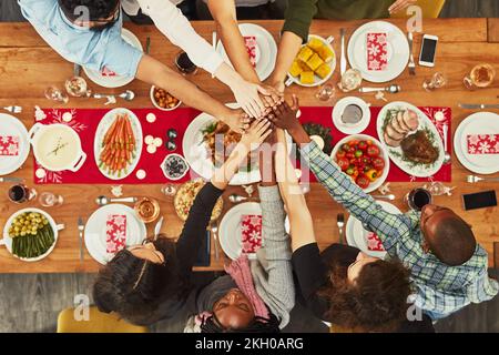 Weihnachten, High Five und Essen mit einer Gruppe von Freunden, die zusammen an einem Tisch sitzen, um zu feiern. Thanksgiving, Hände und Essen mit einem Team Stockfoto