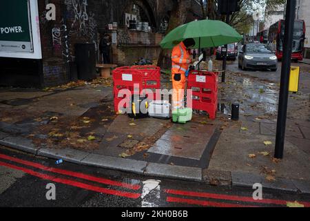 Ein Telekom-Ingenieur eines unbekannten Unternehmens arbeitet am Straßenrand in einer Waterloo-Straße während eines Regenschauers am 23.. November 2022 in London, England. Stockfoto