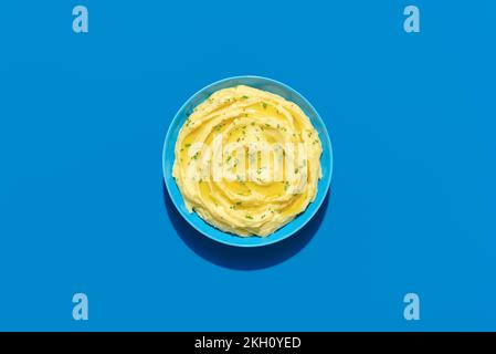 Draufsicht mit einer Schüssel mit Kartoffelpüree, minimalistisch auf blauem Hintergrund. Cremige Kartoffelpüree mit Olivenöl und Petersilie. Stockfoto