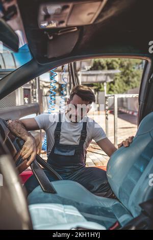 Kfz-Detaillierer, der mit dem Staubsaugen eines schmutzigen Fahrzeuginnenraums befasst ist Stockfoto