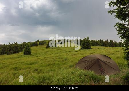 Grünes, leichtes, freistehendes Zelt für 2 Personen auf dem Mravenecnik-Hügel im Gras am Morgen nach dem Regensturm. Jesenik-Gebirge, tschechisch Stockfoto