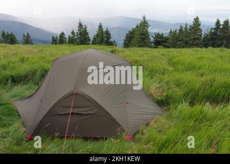 Grünes, leichtes, freistehendes Zelt für 2 Personen auf dem Mravenecnik-Hügel im Gras am Morgen nach dem Regensturm. Jesenik-Gebirge, tschechisch Stockfoto