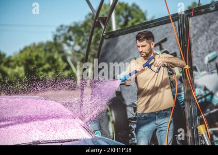 Tankwart wäscht ein Kundenauto mit professioneller Ausrüstung Stockfoto