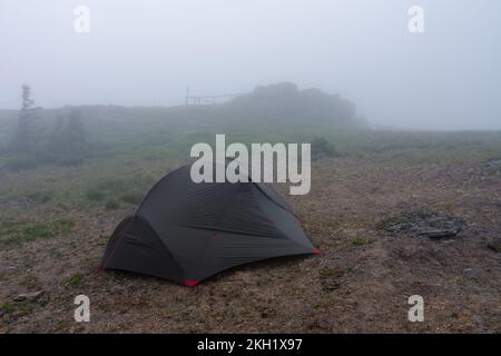 Grünes, leichtes, freistehendes Zelt für 2 Personen auf einem Hügel im Gras am Abend nach dem Regensturm. Jesenik-Berge, Tschechische Republik Stockfoto