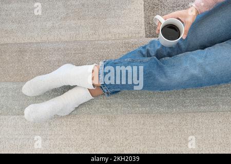 Ein Mädchen auf Teppich ohne Schuhe trinkt Kaffee in ihrem bequemen Zuhause Stockfoto