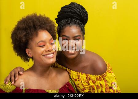 Porträt zweier Frauen vor gelbem Hintergrund. Sie tragen gelbe und rote Kleidung. Stockfoto