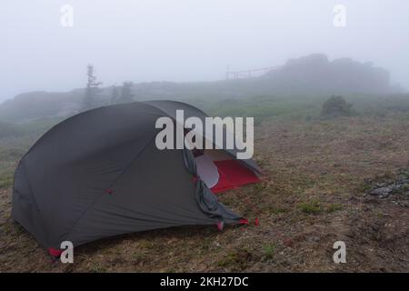 Grünes, leichtes, freistehendes Zelt für 2 Personen auf einem Hügel im Gras am Morgen nach dem Regensturm. Jesenik-Berge, Tschechische Republik Stockfoto