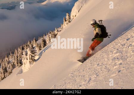 Snowboarder, die sich in Tiefschneepulver bergab auf einem steilen Hang in den Bergen bewegen. Freeride, Wintersport im Freien, Schneewirbel in der Luft Stockfoto